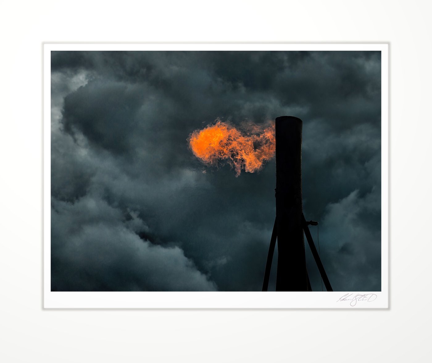 A gas flare burning against dark storm clouds