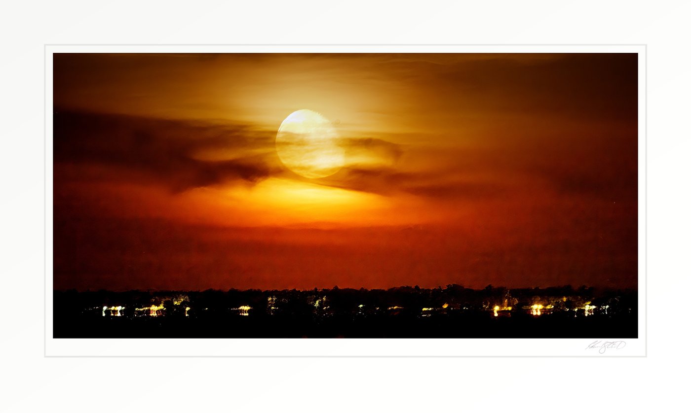A hazy full moon rising in an orange sky above the lights of Caseville