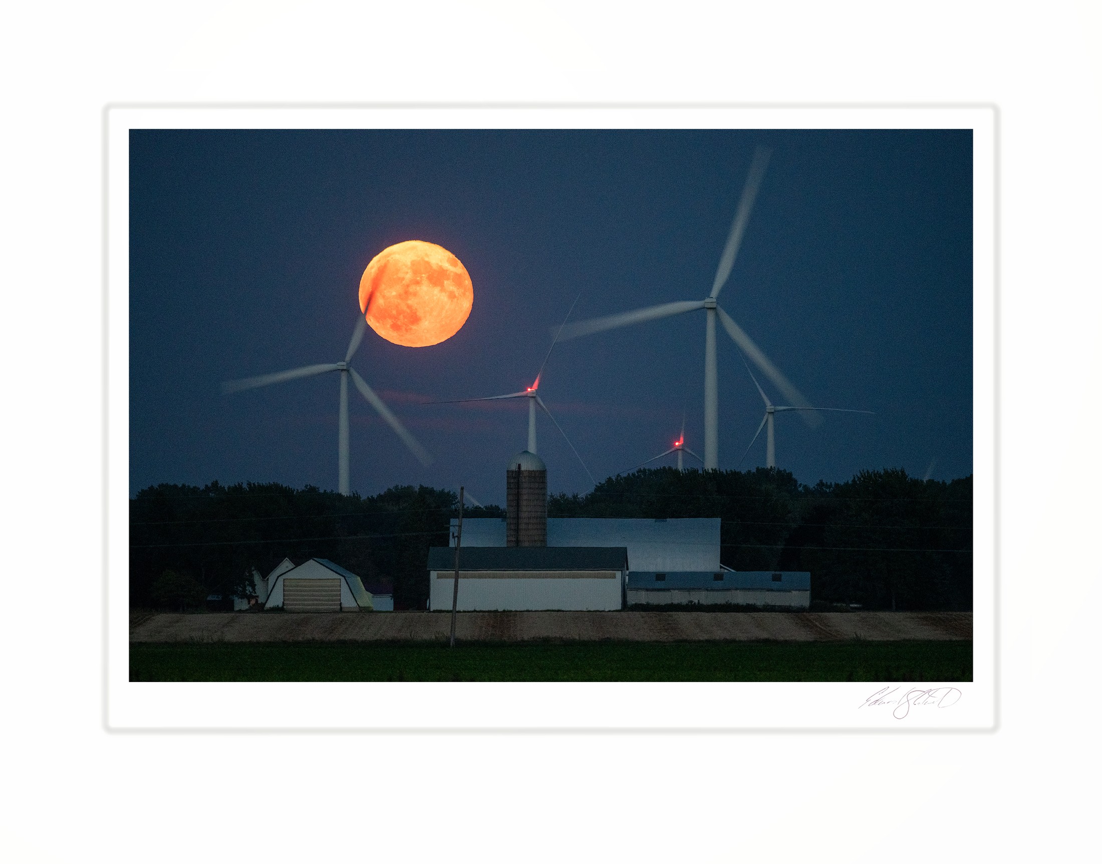 A supermoon rising orange behind wind turbines over a farm
