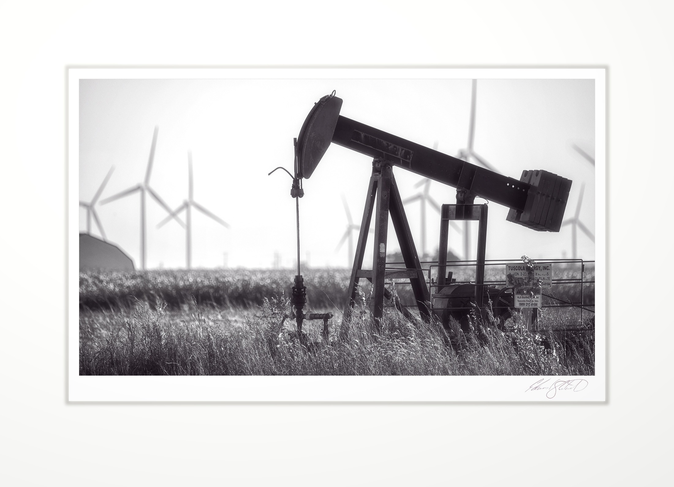An oil pumpjack with wind turbines behind it